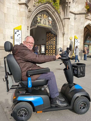 Ein älterer Herr sitzt vor dem Rathaus auf einem Elektromobil